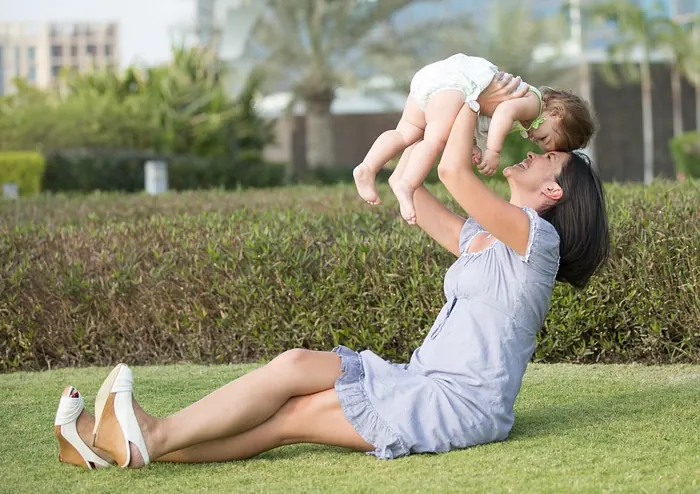 Mãe sentada na grama erguendo o bebê nos braços